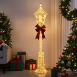 Decorative Christmas lamp post with lights and a bow, surrounded by trees and presents in a room.