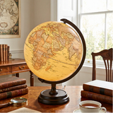 World globe on a wooden desk with books and a cup of tea in a home office setting.
