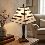 Decorative table lamp with stained glass shade on a wooden surface, with books and a vase in the background.