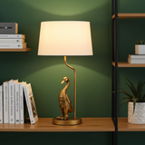 Decorative lamp with a gold base shaped like a duck on a wooden surface against a green wall.