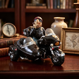 A decorative figurine of a bearded man riding a black sidecar motorcycle, displayed on a dark wooden shelf with vintage books, a clock, and a framed map.