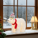 Decorative polar bear with lights on a windowsill with a snowy scene outside.