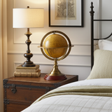 Decorative globe on a nightstand next to a bed with a lamp and framed picture.