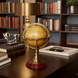 Decorative globe on a wooden desk with books and a lamp in the background