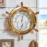 Brass thermometer and barometer on a wooden wall with coastal decor.