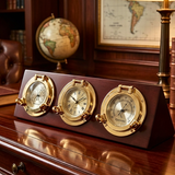 Three gold weather station units on a wooden stand with a globe and map in the background.