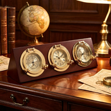 Decorative nautical clock and barometer set on a wooden desk with books and globe in the background.