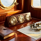 Nautical-themed desk setup with a clock, barometer, and thermometer on a wooden surface.