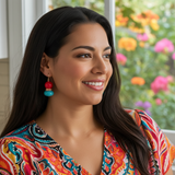 Woman wearing colorful earrings and a patterned top with flowers in the background
