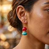 A close-up of a woman's ear wearing a dangling earring with a sterling silver hook, a red coral round bead, a turquoise bead, and a double sterling silver rounds in between.