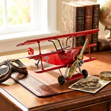 Red model airplane on a wooden desk with books and a globe in the background