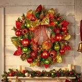 A large festive Christmas wreath hanging on a white wood paneled wall above a decorated mantel. The wreath is decorated with green pine branches, red and gold ornaments, pinecones, and a large red and gold bow.