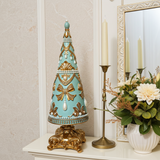 Decorative Christmas tree with gold and blue accents on a shelf with candles and flowers.