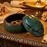 Decorative scarab beetle box with hieroglyphics on a wooden surface with a lamp and papers in the background.