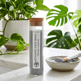 Glass jar of activate face mask with a wooden cap on a marble surface with plants in the background