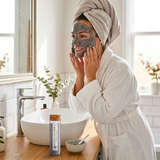 Woman applying facial mask in a bathroom with a product on the counter.