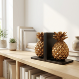 Gold pineapple bookends on a wooden shelf with books and plants in the background