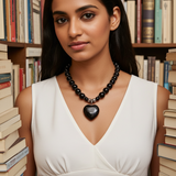 Woman wearing a black agate necklace with a heart pendant in front of bookshelves