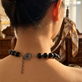 Person wearing a black beaded necklace with a silver clasp on their neck.