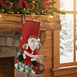 A festive Christmas stocking hanging from a rustic wooden mantel decorated with pine branches, pinecones, and warm string lights. The stocking is red with white snowflake details, a plush Santa Claus figure, and a plaid lower section, set against a cozy fireplace with a snowy window in the background.