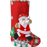 A festive Christmas stocking with a Santa Claus design hangs from a decorated fireplace mantel. The mantel is adorned with a green and white frosted pine garland, red and gold ornaments, candles, and a gold reindeer ornament.