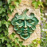 Green man face sculpture on a stone wall with ivy and flowers