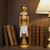 Gold nutcracker figurine with a crown on a shelf with books and a lamp.