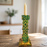 Decorative candle holder with intricate green and gold design on a wooden table.
