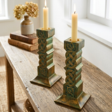 Decorative candle holders with candles on a wooden surface near a window.