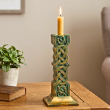 Decorative candle holder with a candle on a wooden surface next to a plant and book.