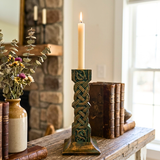 Decorative candle holder with a lit candle on a wooden surface with books and a vase.