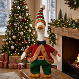 Decorative goose figurine in festive attire with Christmas tree and fireplace in the background