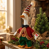 Decorative goose figurine in festive attire on a Christmas-themed setting with a small tree and decorations.