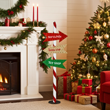 Decorative sign with directional arrows in a festive living room with Christmas tree and fireplace.