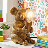 Gold  Koala bear lamp holding a light bulb on a shelf with colorful books and toys.