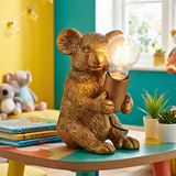 Decorative  Koala bear lamp holding a light bulb on a colorful table with books and plants in the background.