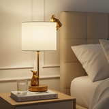 Gold rabbit-shaped lamp on a nightstand next to a bed with white pillows.