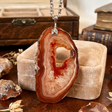 Agate pendant necklace on a wooden surface with books and jewelry box in the background