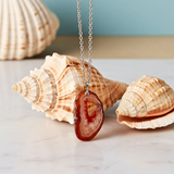Necklace with a red agate pendant on a marble surface with seashells.