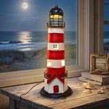 Decorative lighthouse lamp on a wooden surface with a window view of the ocean.