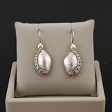Pair of silver earrings on a beige jewelry display pillow against a black background