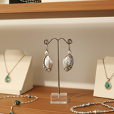 Pair of silver earrings on a stand with necklaces in the background