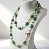 A multi-strand beaded gemstone necklace with green  adventurine stones , small fresh water pearl beads and fancy agate , and a sterling silver bird clasp, displayed on a light gray jewelry bust.