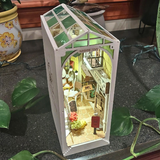 Model of a miniature town inside a glass box on a dark surface with plants around.