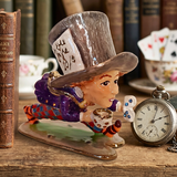 Decorative figurine of a character from 'Alice in Wonderland' with a top hat and pocket watch on a wooden surface.