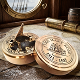 A round brass sundial compass with its lid open, placed on a vintage map with a telescope and porthole window in the background. The lid is engraved with 'THE MARY ROSE LONDON 1511 - 1545' and features a ship illustration.