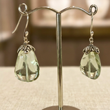 Green teardrop earrings on a stand with a blurred background
