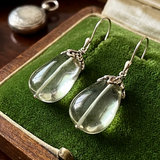 Teardrop-shaped earrings with silver hooks on a green fabric background