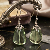 Green teardrop earrings with silver hooks on a dark surface.