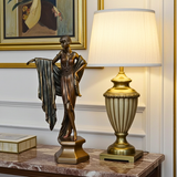 Bronze statue of a woman and decorative lamp on a marble surface with a painting in the background.